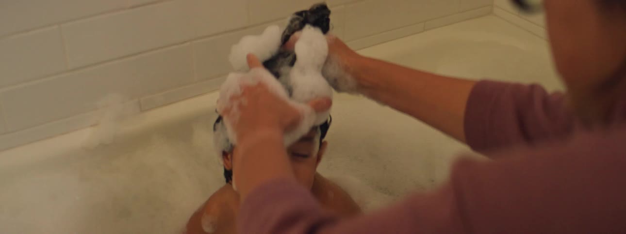 A woman shampoos her daughters hair during a bath