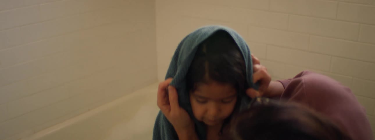 A mother wraps her daughter in a towel after a bath and kisses her