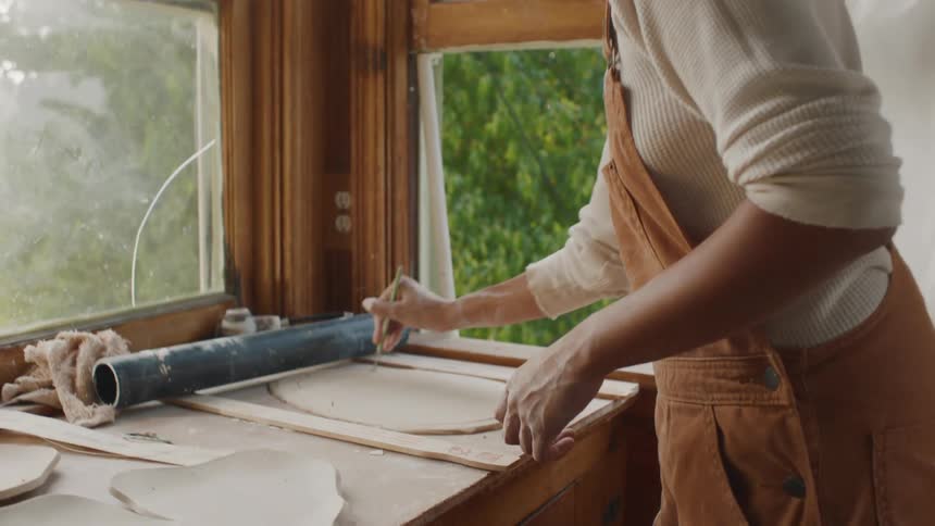 A women using a toll to sculpt next to open windows on a bright day