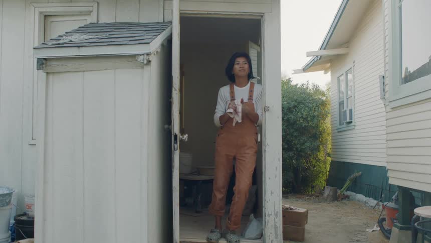 A woman wipes her hands on a towel while standing in the doorway of her shed
