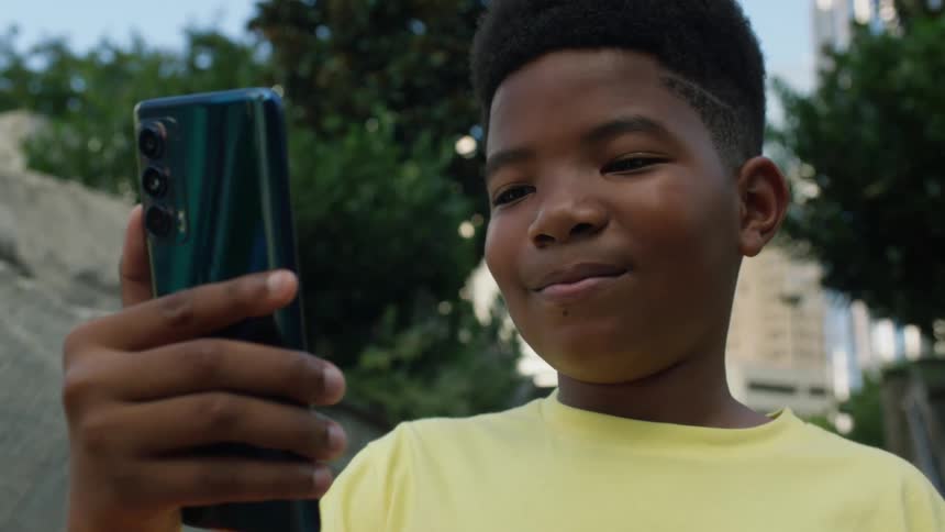 A boy smiles while looking at his smartphone in a park