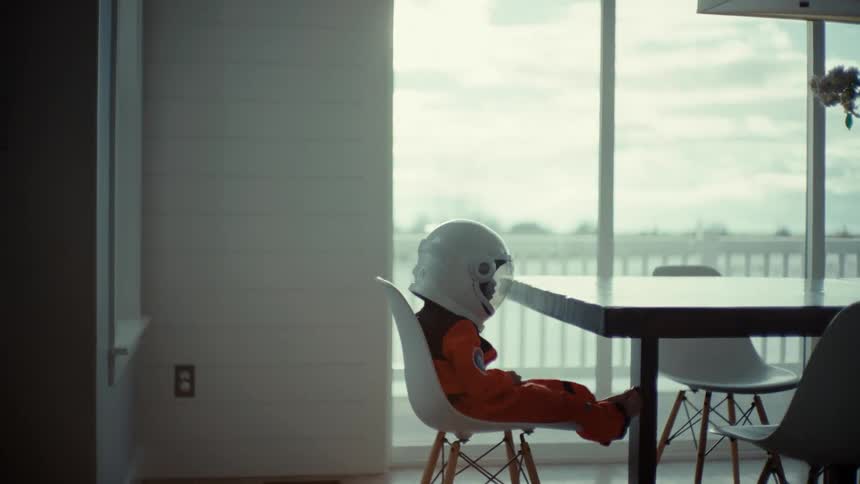 A young child sits at a table at home in an astronaut outfit