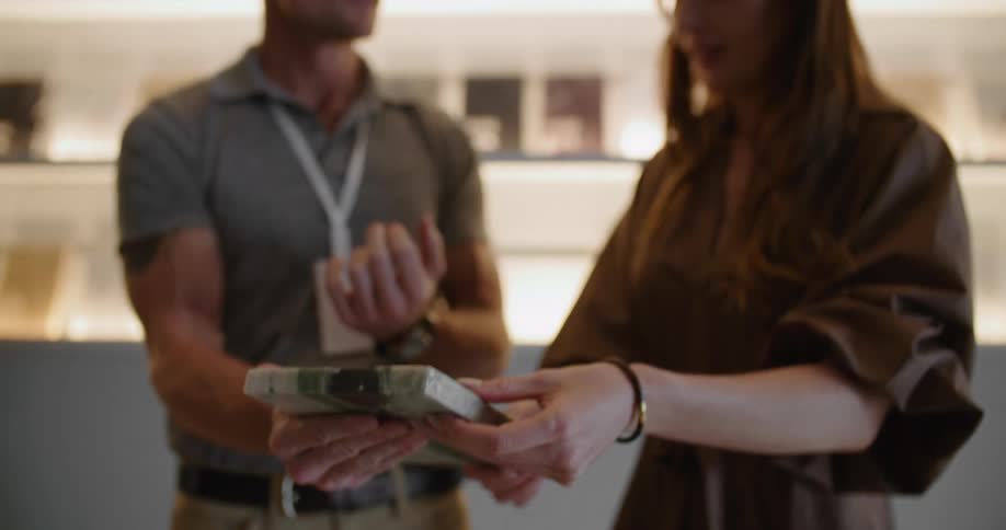 A delivery man is standing next to a woman inside her place of business as he holds a device showing her the information and they talk