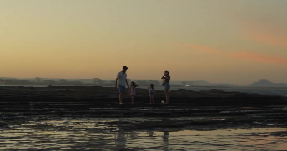 Parents hold their daughters hands while they play on the beach