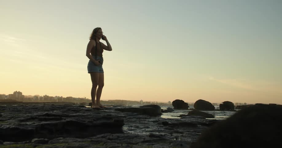 A woman talking on the phone standing on rocks on the coast