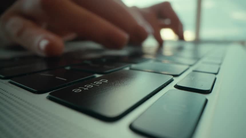 A person is typing on a laptop keyboard and hits the delete key several times in a row