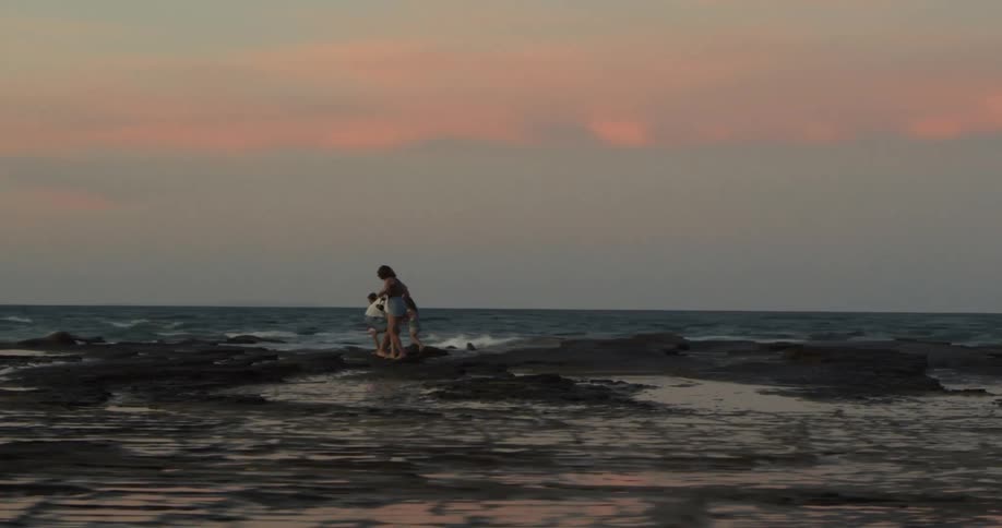 A family walks along rocks on the shore