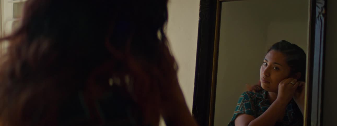 A woman puts on earrings while looking in a mirror