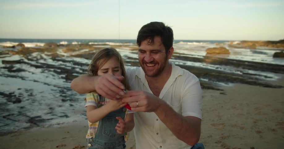 A man helps his daughter fly a kite on the beach