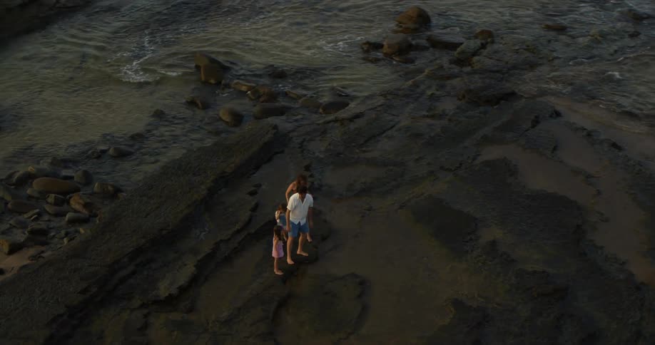 A family walks across tide pool on a black sand beach