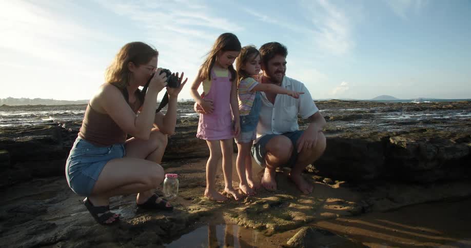 Father mother crouching beside daughters take photos on muddy beach next to the sea