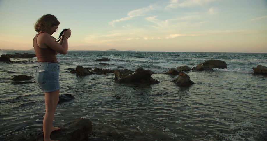 Woman balancing on boulder in water at shore takes pictures