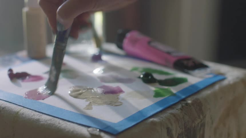 An artist is mixing paint colors on cardboard with a paint brush