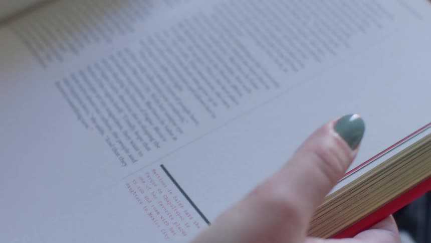 A woman wearing green nail polish is holding a book and flipping through the pages