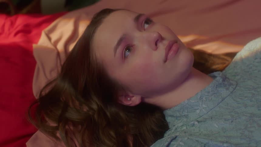 Young woman with long hair laying on the bed feeling sad and hopeless shaking her head