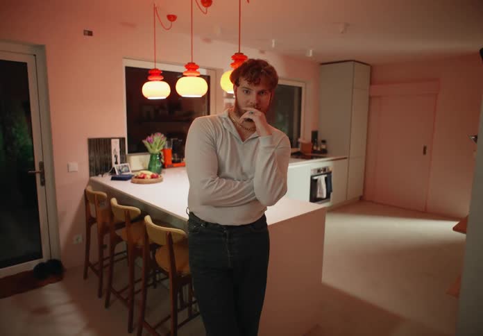 A man leans against a kitchen counter at home and rests his hand on his face