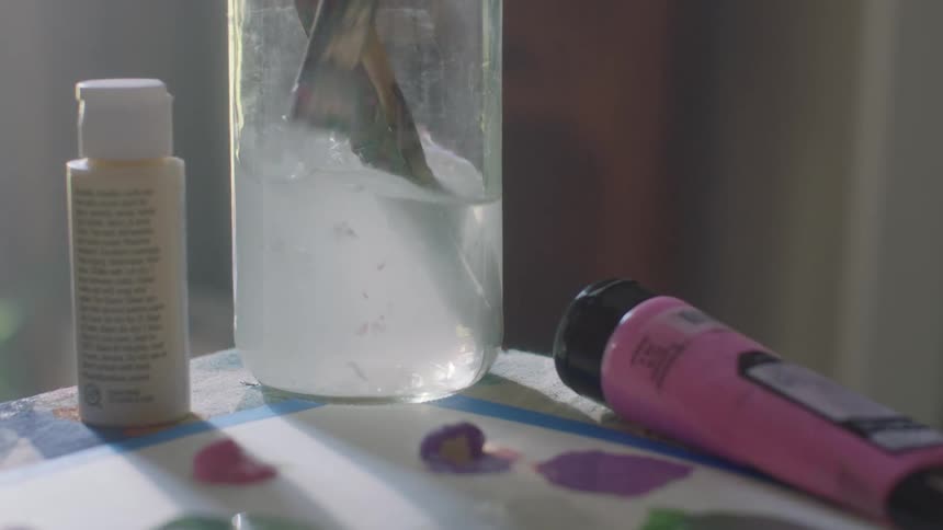 Paintbrush is swished in a glass of water sitting next to paints