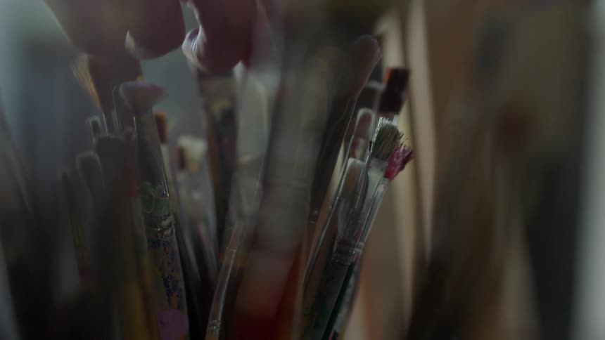 A person grabbing a paintbrush out of a cup