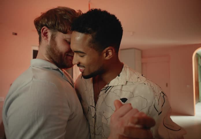 Two men slow dance at home near the kitchen at night