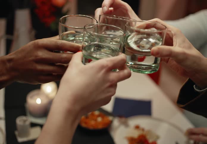 A group of people at a table at home clink their glasses together and cheer one another