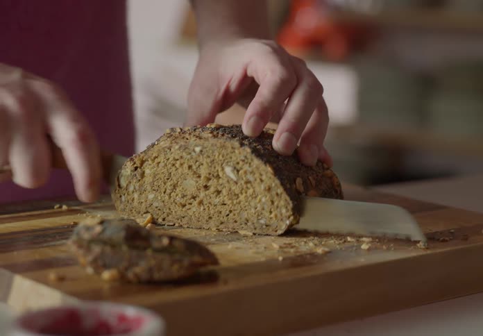 Cose up of a person in the kitchen slicing bread with a bread knife on the cutting board