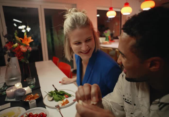 A man smiles and talks sitting at the dining room table next to a female friend