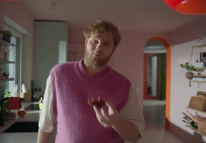 A man is standing in a room holding a bagel and he takes a bite as he looks ahead