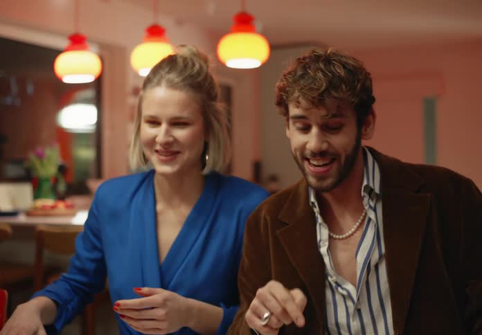 Man with beard and brown blazer kisses blonde woman with blue dress at table eating dinner