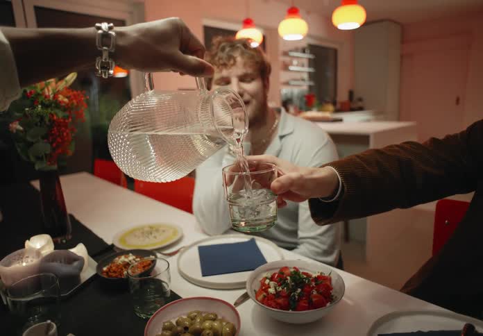 People sit at a counter with a spread of food while one person pours water for another person