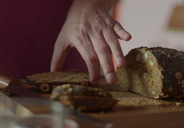 A person cuts a slice of bread and spreads jam on it