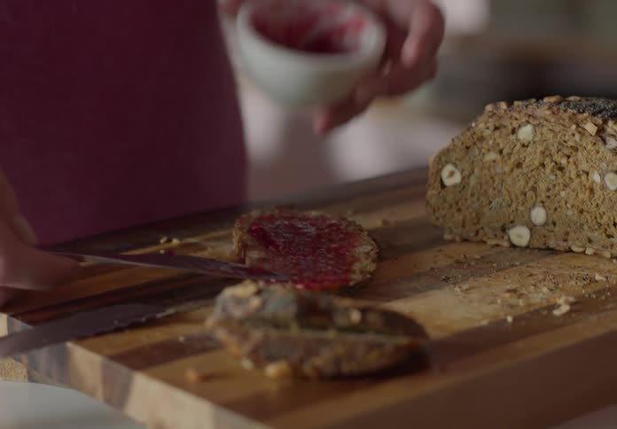 Man spreads jelly on freshly sliced multigrain bread