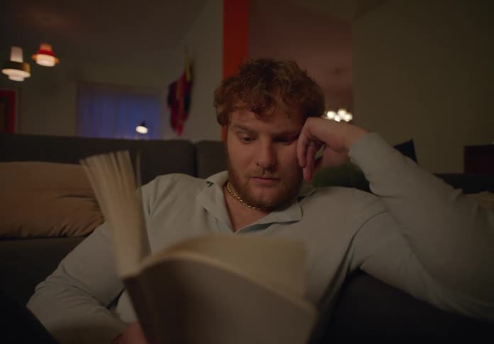 Male redhead leans against couch while reading a book