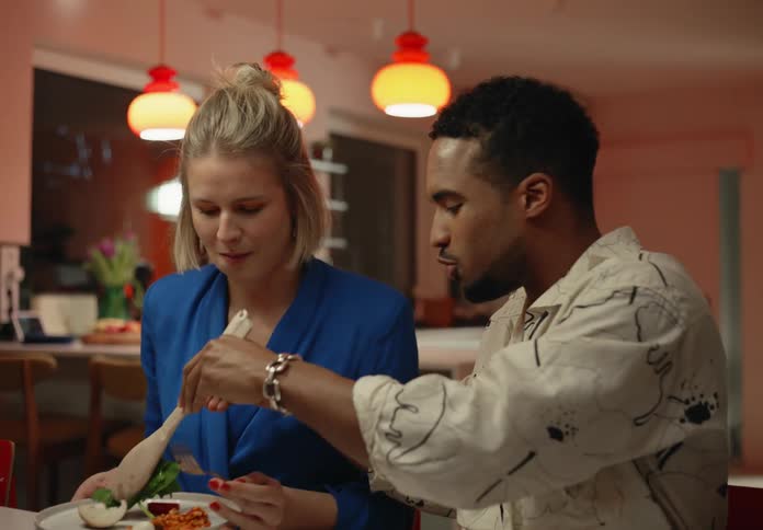 A black man is serving salad to a white woman as they share dinner together in a home dining room