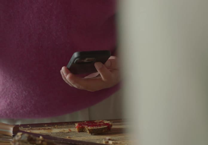 Man with white t shirt and pink sleeveless pullover takes mobile phone out of his pocket and show it to man in the kitchen