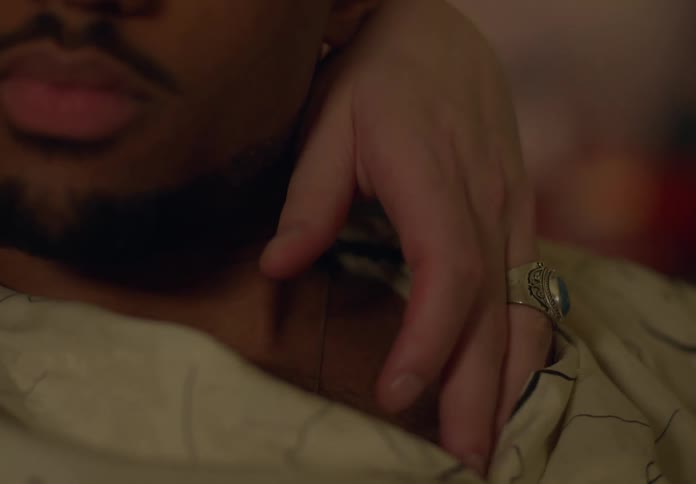 A man is standing behind his boyfriend and reaching into his shirt rubbing his chest with his fingers