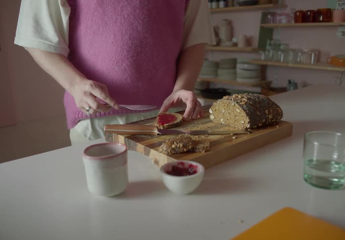 Two people enjoying bread and jam in the kitchen one of them spreading jam on a slice of bread