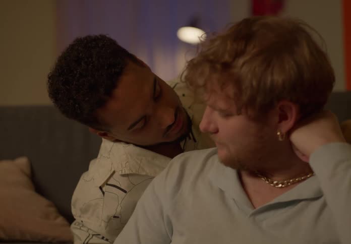 A man kisses his partner on the cheek in their living room