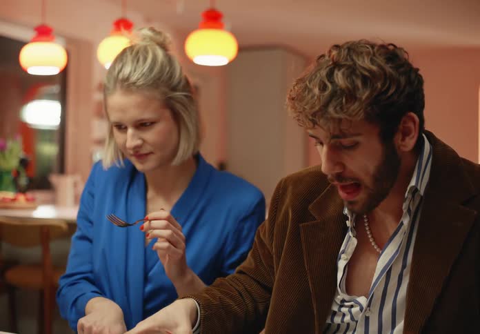 A man is sitting next to a woman at a table as he drinks from his glass and holds his fork as he speaks