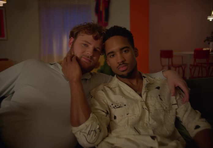Two men cuddle together and nuzzle while sitting on couch in home