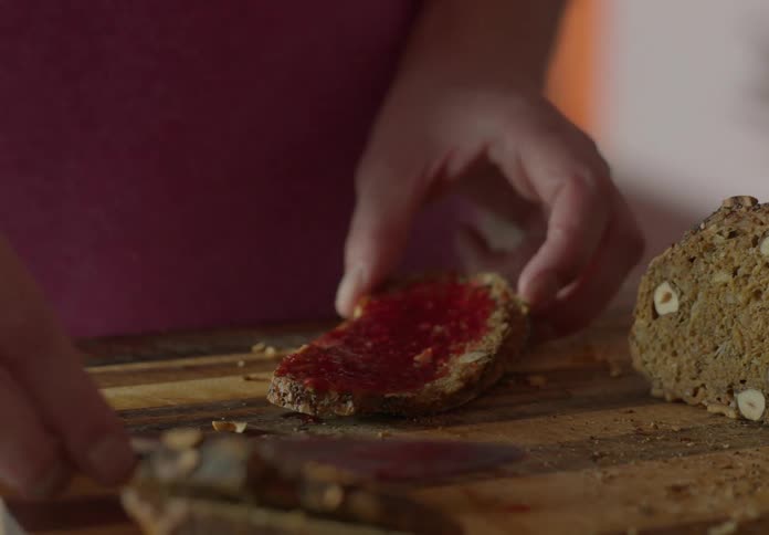 Man with pink t shirt spreads jam on bread in the kitchen