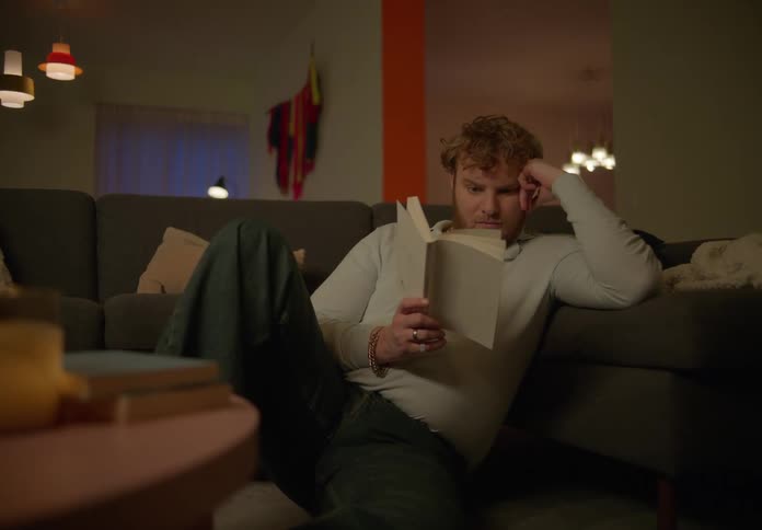 A man is relaxing on the living room couch reading a book