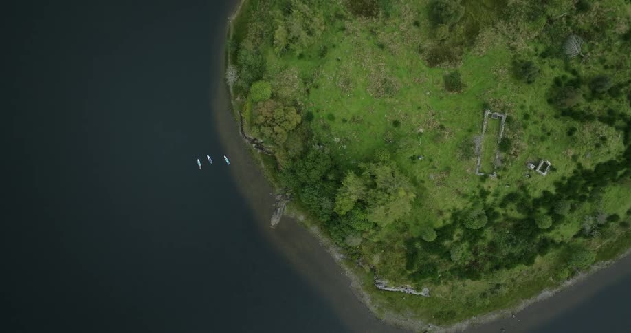 Paddleboarders paddle near the shore of an island with green vegetation and the ruined frame of a building