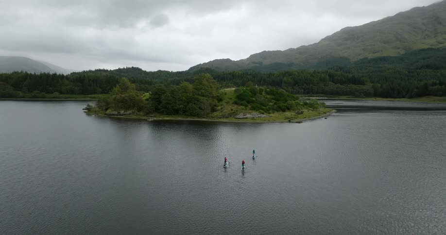 Three people are standup paddleboarding towards an island under a cloudy sky