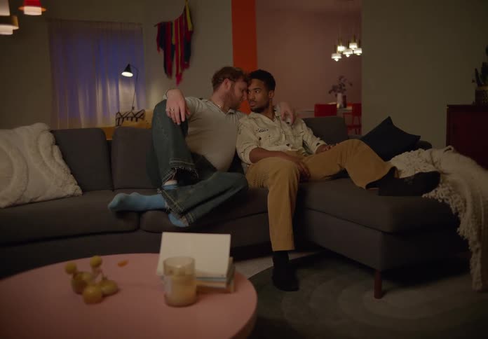 Gay couple sitting on couch hold each other and looking into each others eyes lovingly