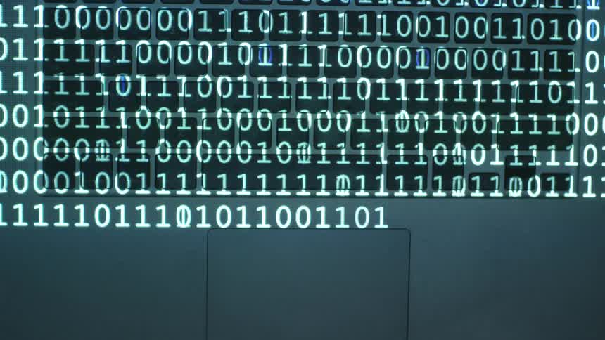 Lines of ones and zeroes flash on a laptop keyboard