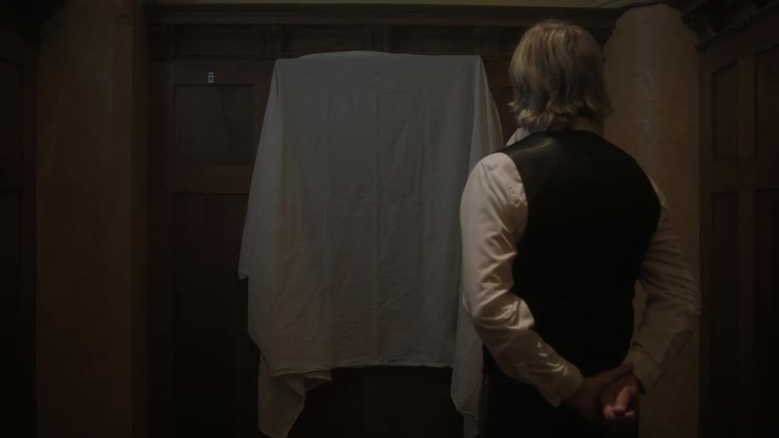 A man stands in front of a picture with a cloth over it