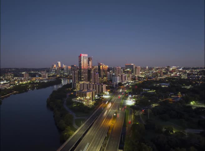 Traffic moves over a bridge in and out of a metropolitan city along the coast with tall buildings and skyscrapers on the city skyline
