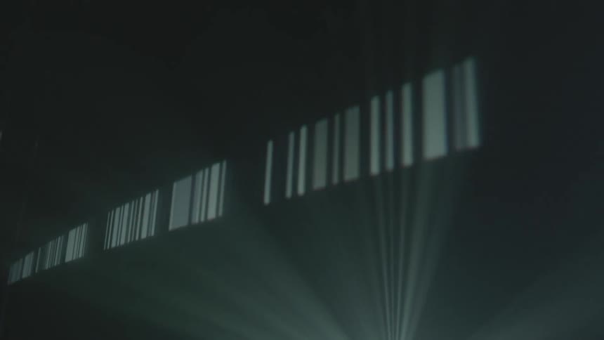 A strip of barcode-like light is projected across a dark surface
