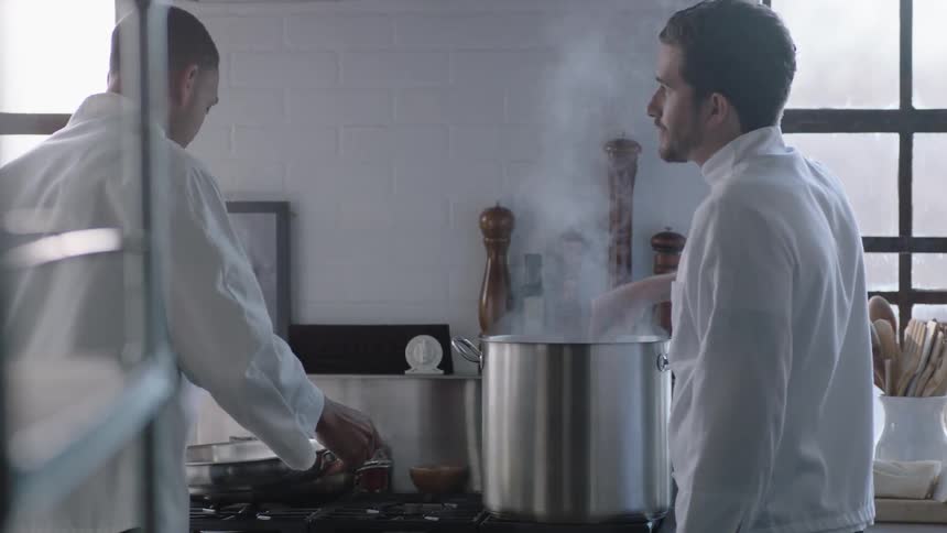 Two chefs stand cooking at a stove in a kitchen