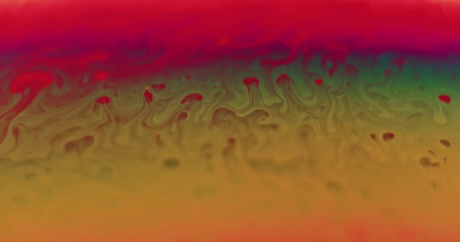Ridges and droplets form in an organic yellow and red surface with blending colors green and orange as it moves